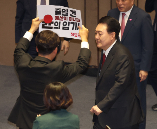 지난 2023년 10월31일 국회 본회의장에서 시정연설을 마치고 퇴장하자 강성희(왼쪽) 진보당 의원이 '줄일 건 윤의 임기'라고 적힌 손팻말을 들어 항의를 표하고 있다. 강성희 의원은 2024년 1월18일 전북 전주에서 열린 전북특별자치도 출범 행사에서 전북 지역구 국회의원으로서 윤 대통령과 악수 도중 손을 놓지 않고 정치 구호를 연발하다가 대통령 경호원들에게 강제로 퇴장당하기도 했다.<연합뉴스 사진>
